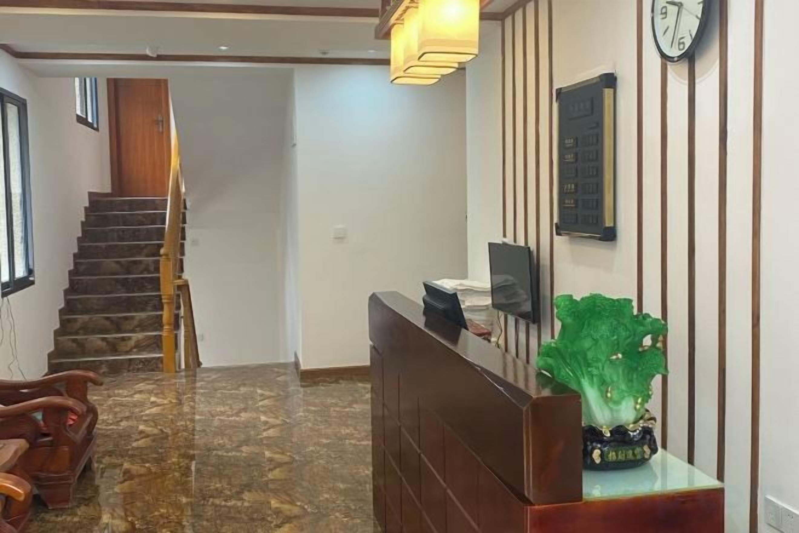 Zona de recepción con un mostrador de madera, un reloj en la pared y una escalera al fondo.