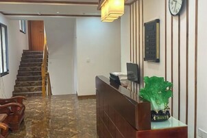 Zona de recepción con un mostrador de madera, un reloj en la pared y una escalera al fondo.