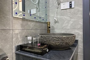 A bathroom with a large, textured basin, a glass container, and a small black tray. - Happy Heart Inn (Dafang)