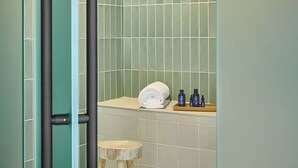 Une salle de bain moderne avec une douche à parois de verre, un tabouret en bois et des articles de toilette disposés sur un plateau.