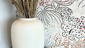 A white vase with dried wheat stalks on a grey countertop against a wall with a floral pattern. - Toile & Bubble Orange and Clove Suite (Forsyth County)