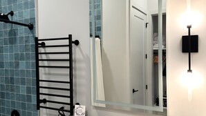 A modern bathroom with a large mirror, a towel rack, a sink, and a small potted plant. - Toile & Bubble Orange and Clove Suite (Forsyth County)