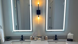 A bathroom with two sinks, a mirror, and a wall-mounted light fixture.