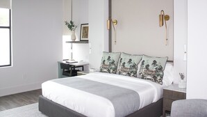 Un dormitorio moderno con una cama grande, un escritorio y una silla. Hay luces empotradas en la pared y una lámpara en el techo.
