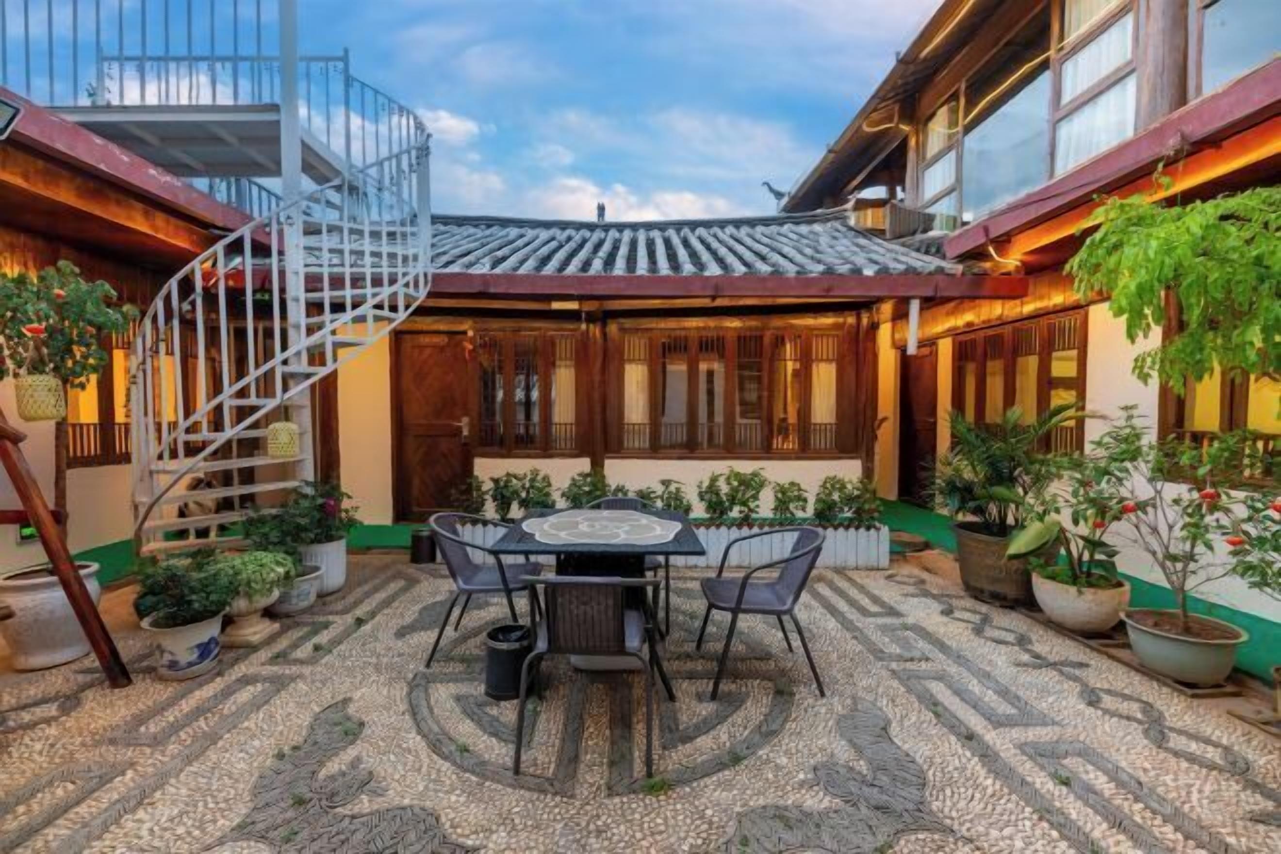 Un patio con suelo de baldosas, una mesa con sillas, plantas en macetas y una escalera de caracol.