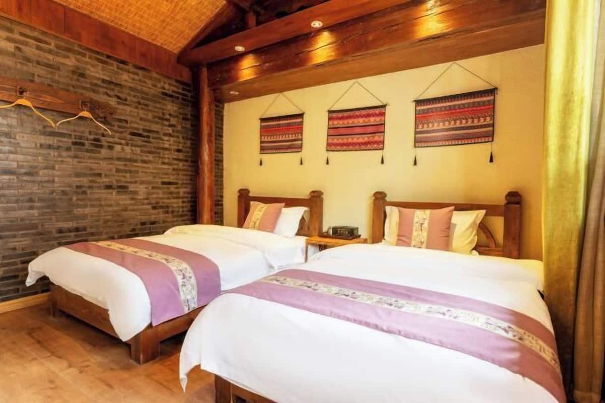 Une chambre avec deux lits, des têtes de lit en bois, un mur en briques et une tapisserie suspendue.