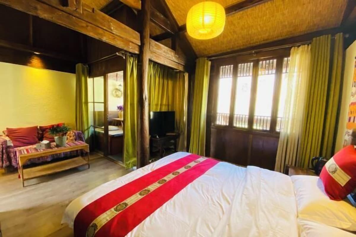 A room with a large bed, a sofa, a television, and a window with curtains.