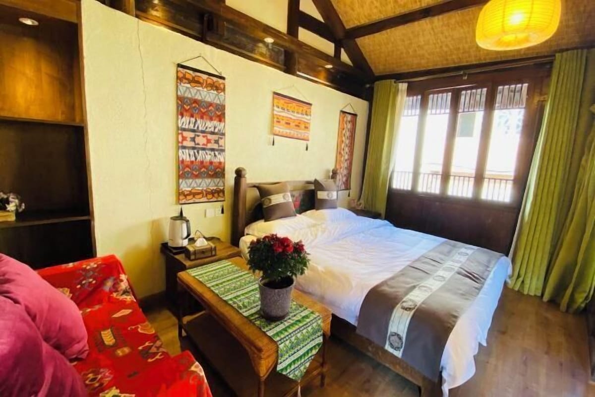 A bedroom with a bed, a bedside table with a lamp, a bench, and a potted plant.