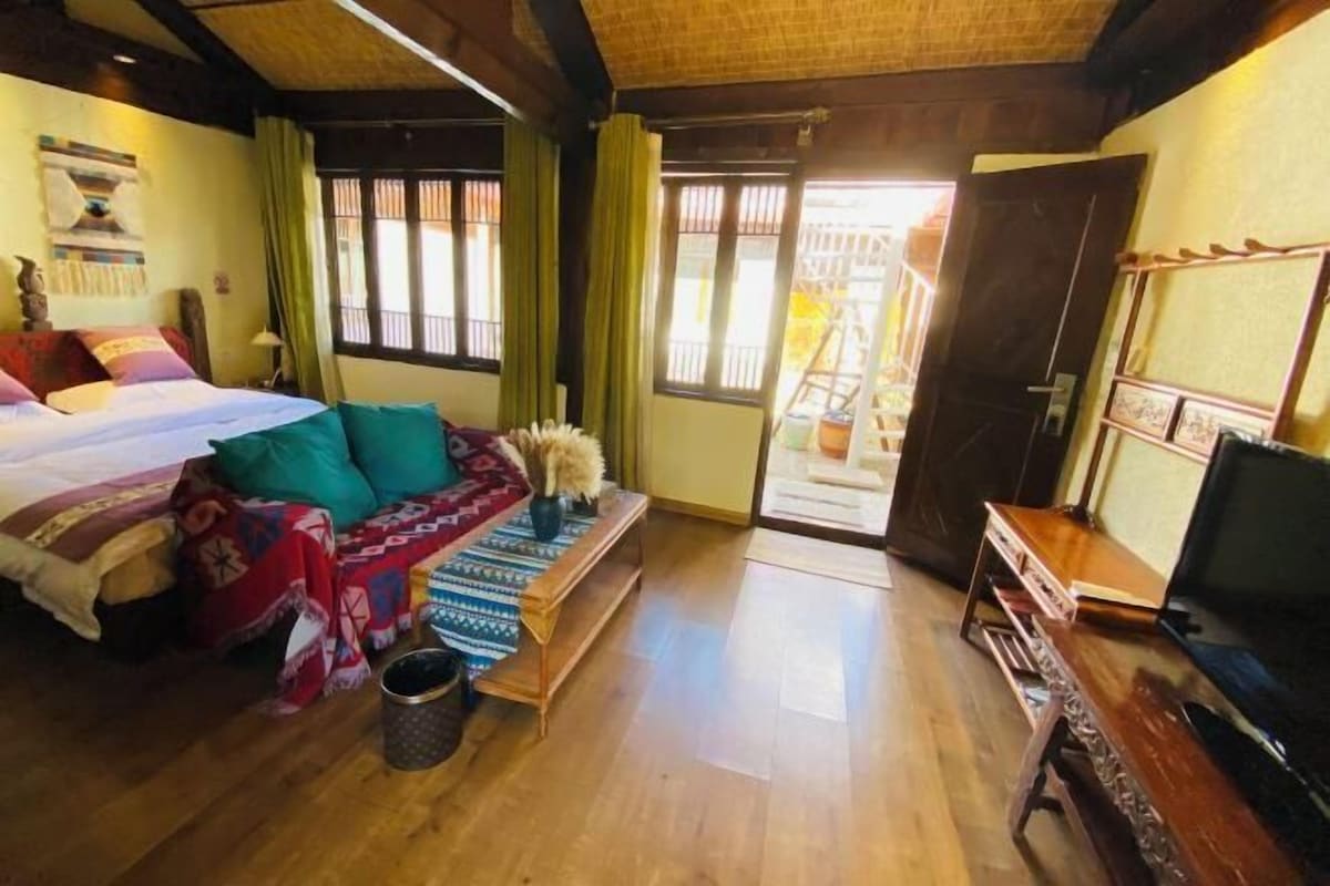 A room with a bed, a small table with a vase, a television, and a door leading outside.
