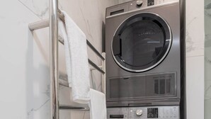 Lavadora y secadora de acero inoxidable, compacta y fijada a la pared, en un baño con baldosas de mármol blanco.
