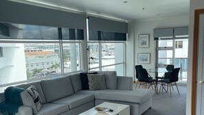 Un salon moderne avec un canapé d’angle gris, une table basse blanche et un tapis à motifs.