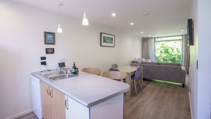 Una cocina moderna con lavavajillas integrado, un comedor con mesa y sillas, un sofá y un ventanal con vistas a zonas verdes.