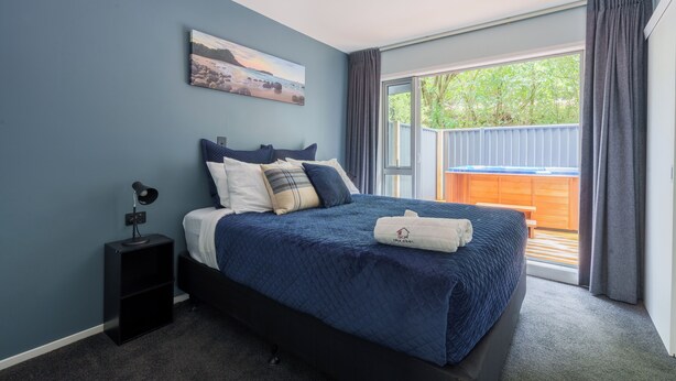 Un dormitorio con cama, mesita de noche, un cuadro en la pared y vistas al exterior.