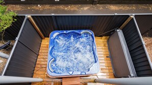 Un jacuzzi en un recinto exterior con terraza de madera y barandillas metálicas.