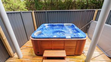A hot tub with a wooden bench in a fenced outdoor area.
