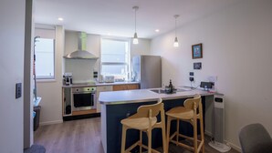 Una cocina moderna con una isla central, taburetes de bar, horno empotrado y refrigerador.