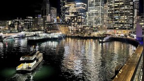Überblicksaufnahme einer beleuchteten Stadtlandschaft bei Nacht, mit Gebäuden und einem Boot an einem Steg.