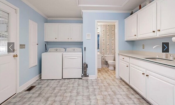 A laundry room with two washing machines, a dryer, and a vacuum cleaner.