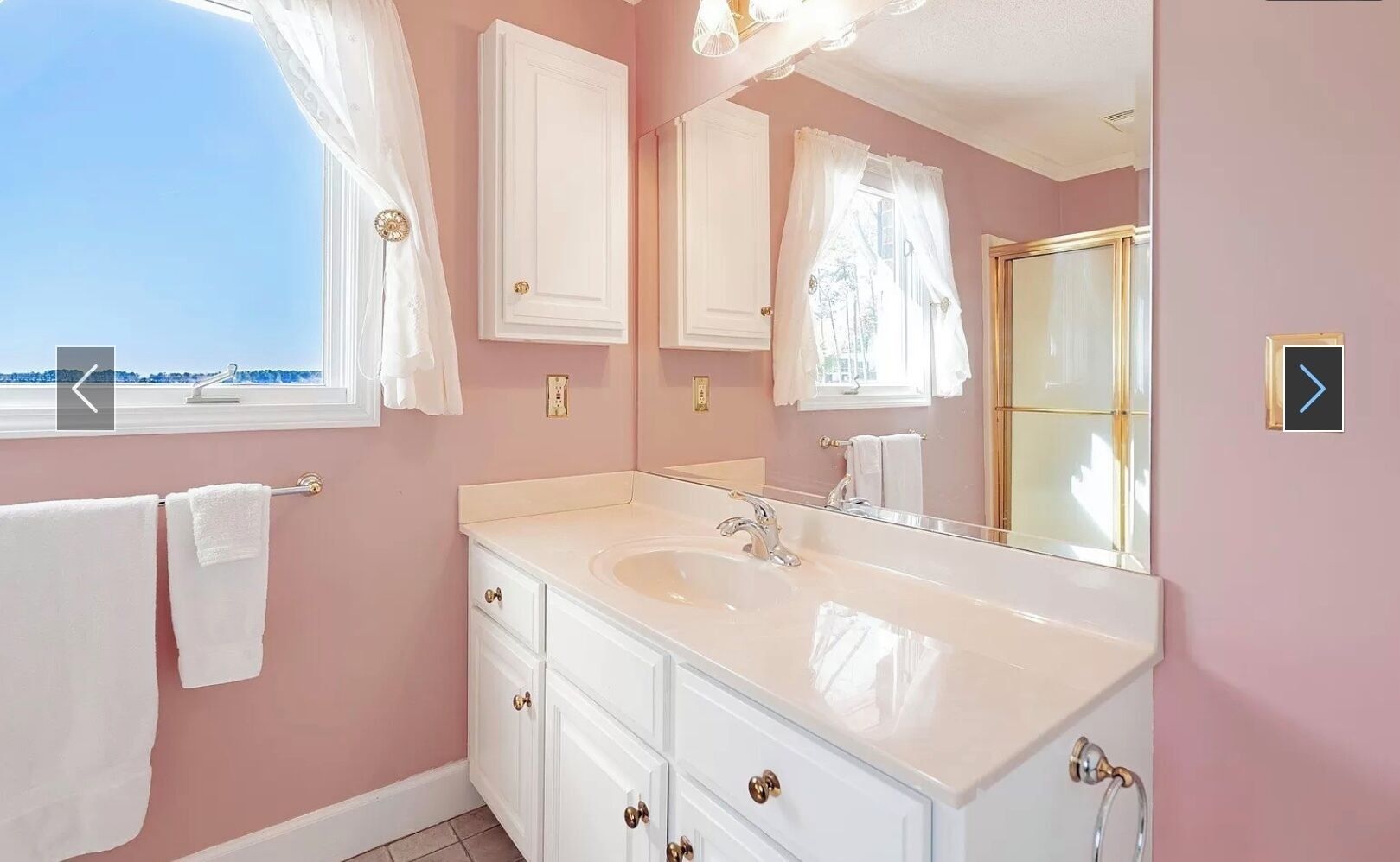 A bathroom with a white vanity, a large mirror, and a window with curtains.