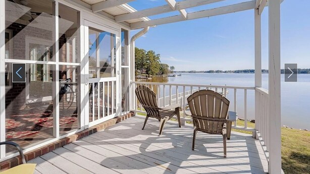 A covered deck with two Adirondack chairs, a glass door leading to a patio, and a view of a lake.