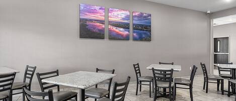 Un restaurante con una decoración moderna, que presenta un comedor con mesas y sillas, y una pared con tres cuadros de paisajes.