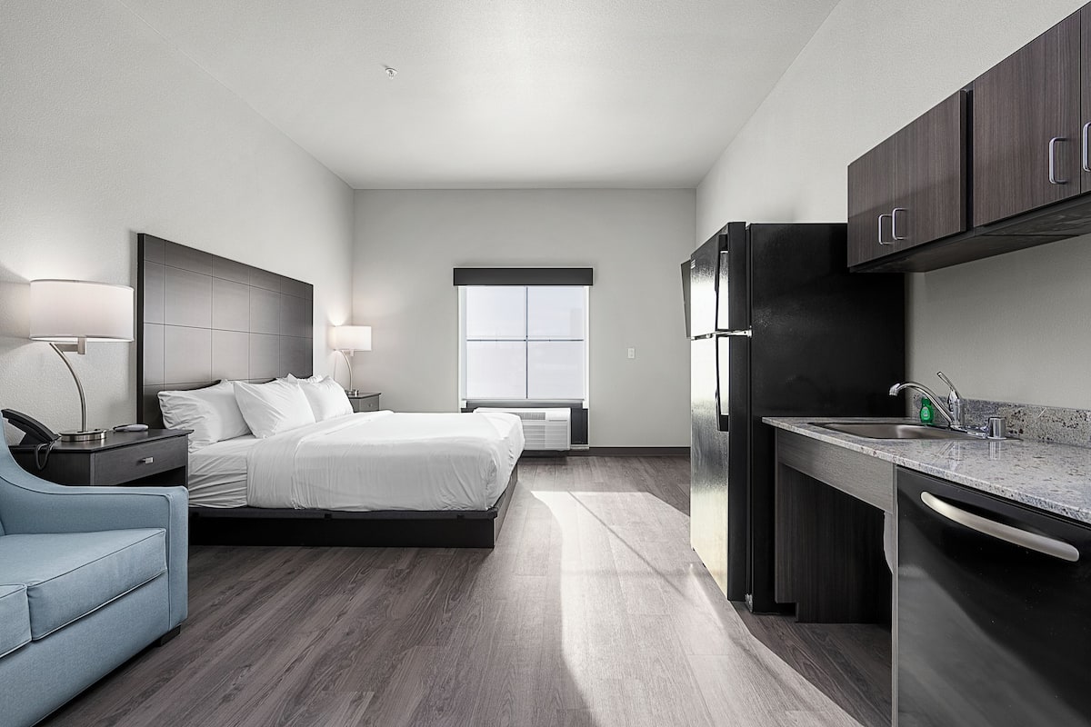 A modern hotel room with a bed, bedside table, lamp, and a view of the outside.