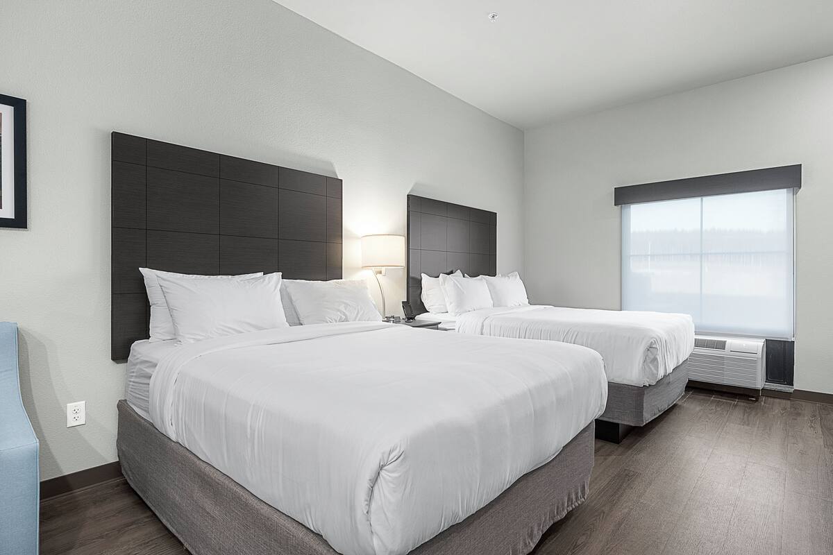 A hotel room with two beds, a large window, and a modern design.