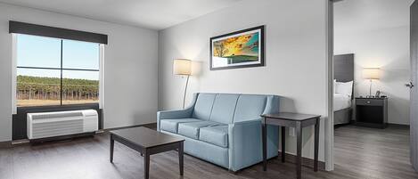A modern living room with a blue sofa, a coffee table, a side table, a framed picture on the wall, and a large window with a view of a field.