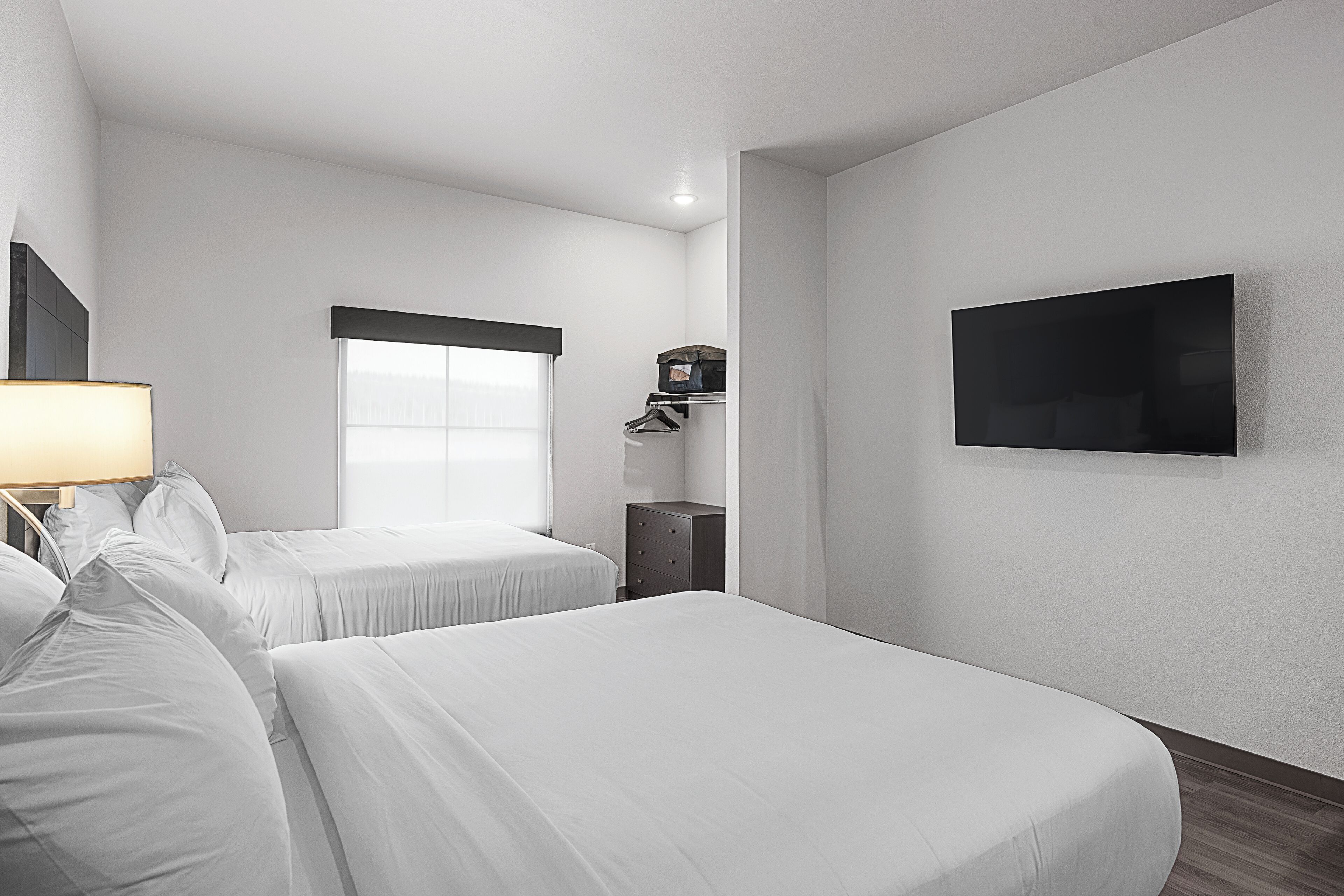 A hotel room with two beds, a TV, a dresser, and a window.