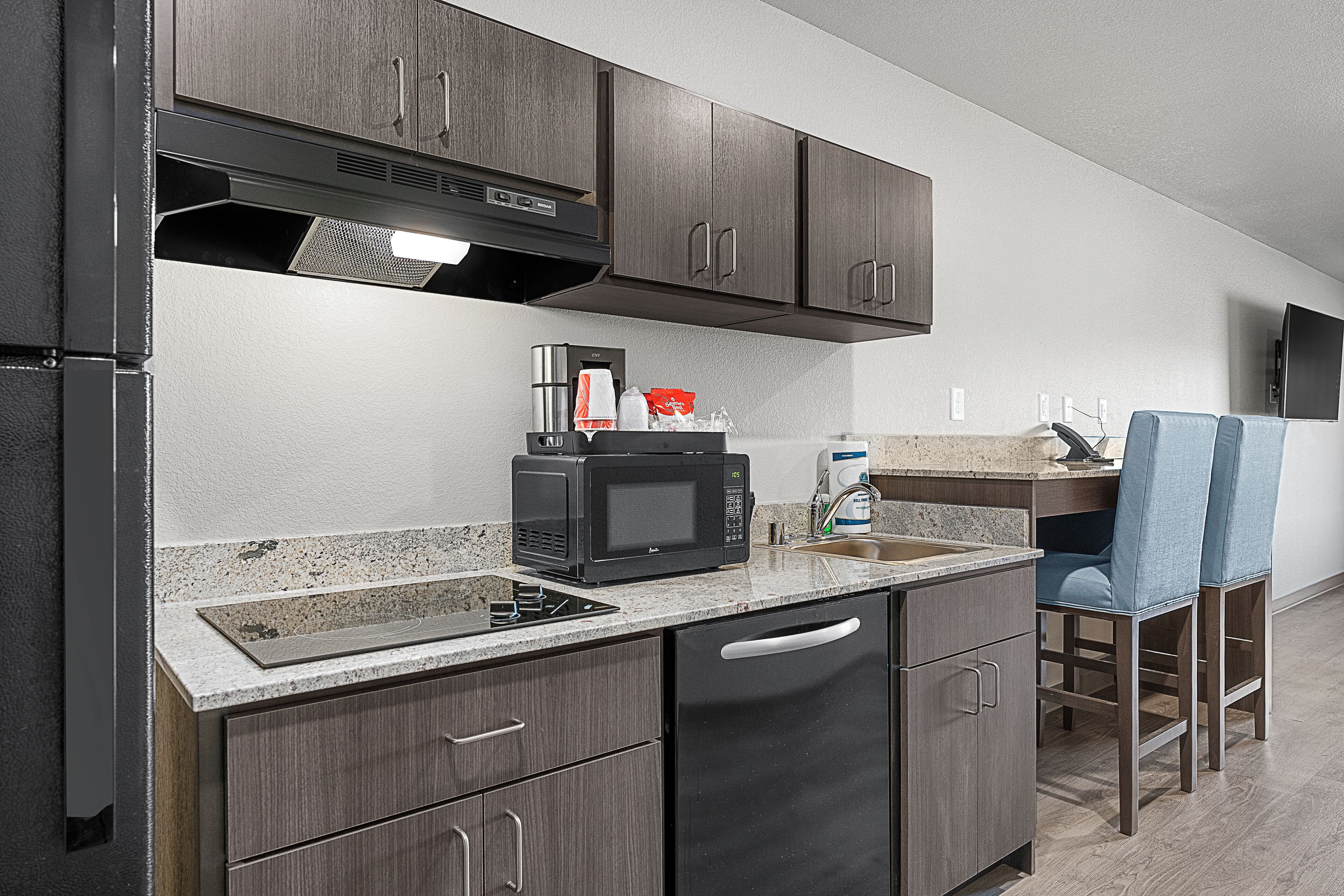 A modern kitchen with dark wood cabinets, a stainless steel microwave, a coffee maker, and a sink.