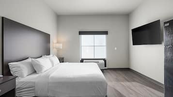 Quarto de hotel moderno com uma cama grande, televisão de tela plana, janela com persianas e ar condicionado integrado.