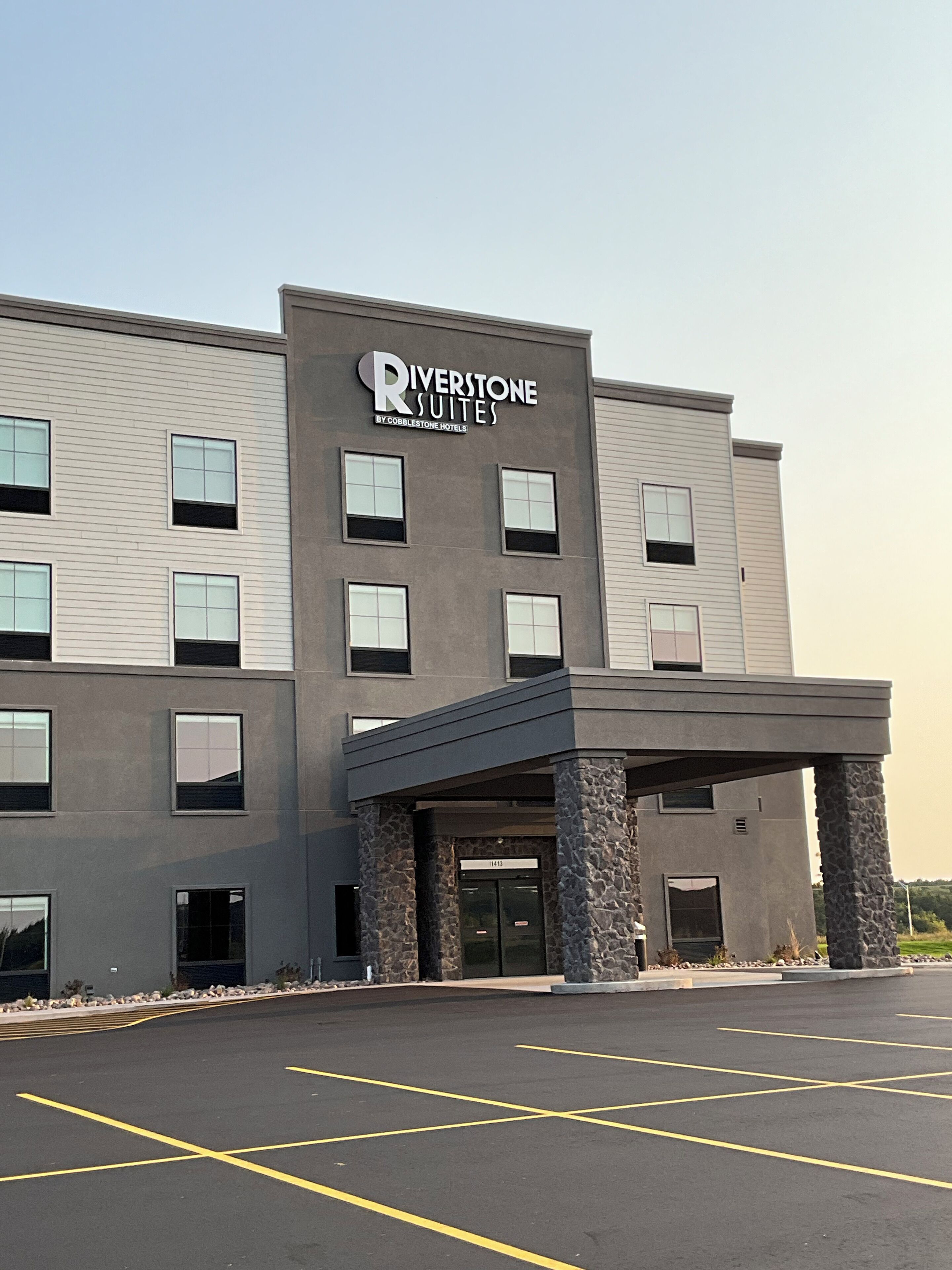 A Riverstone Suites hotel with a modern facade, stone pillars, and a parking lot.