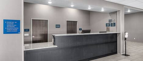 A reception area with a counter, a sign indicating the location of the elevator, and a sign for the business center.