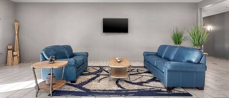 Una sala de estar moderna con dos sofás de cuero azul, una mesa de centro de madera y un televisor montado.