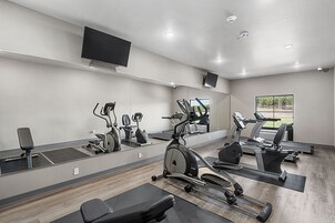 Un gimnasio con máquinas de cardio, espejos y un ventanal grande.