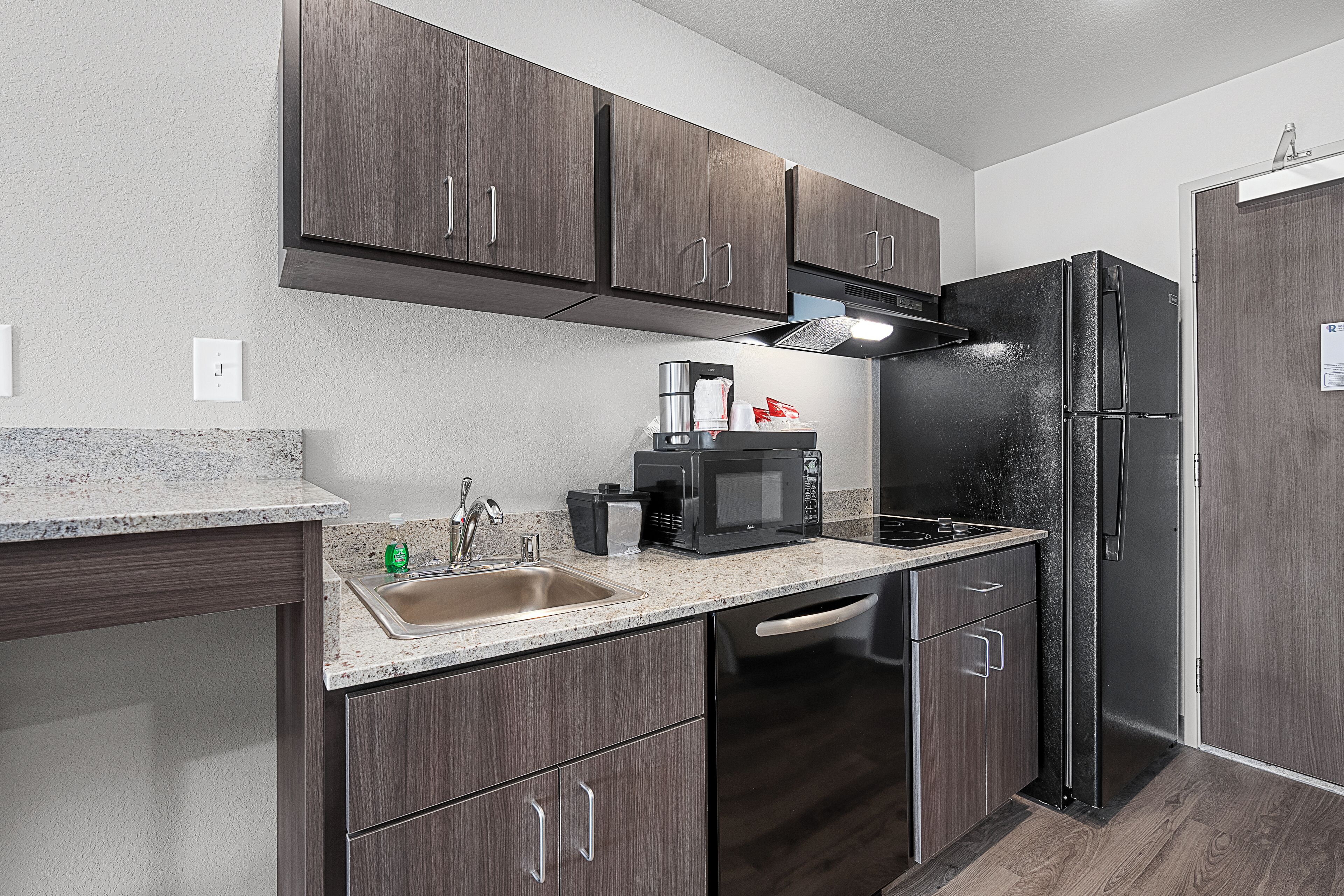 A compact kitchen with dark wood cabinets, a stainless steel refrigerator, a microwave, and a sink with a faucet.