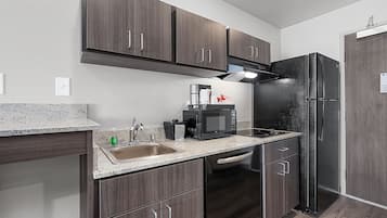 A compact kitchen with dark wood cabinets, a stainless steel refrigerator, a microwave, and a sink with a faucet.
