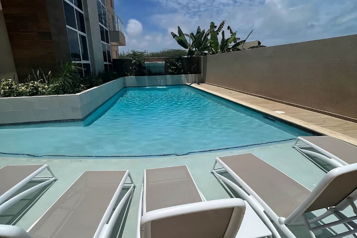 Una piscina con sillones de descanso y vista a un edificio.