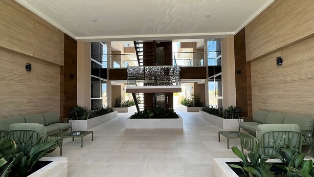 A spacious lobby with a central staircase, modern furniture, and planters. - THE Aracari (Noord)