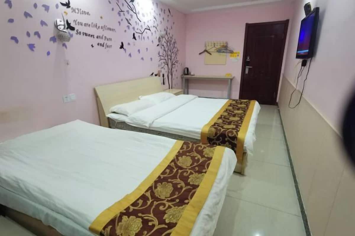 A hotel room with two beds, a TV mounted on the wall, and a decorative wall with a tree and leaves.