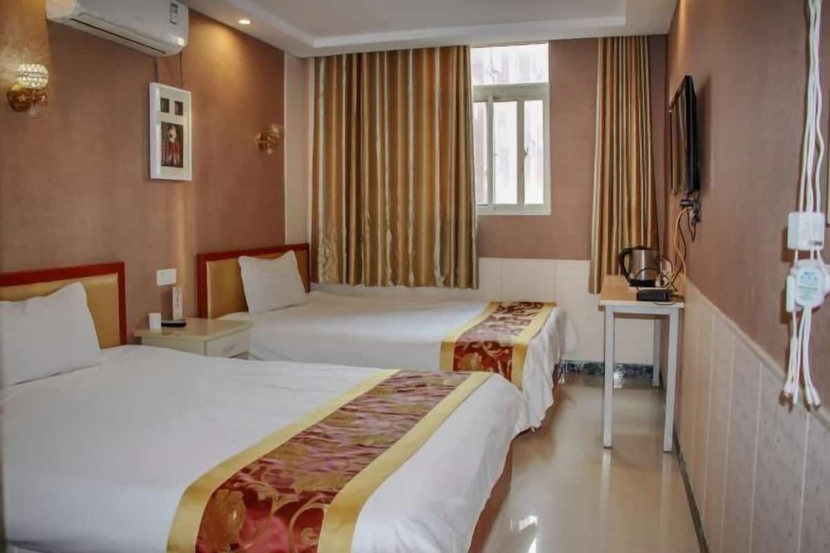 A hotel room with two beds, a small table, a TV, and a window with curtains.