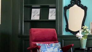 Una poltrona in velluto rosso con un cuscino fiorato blu, un tappeto soffice, una parete color acquamarina e uno specchio con cornice nera.