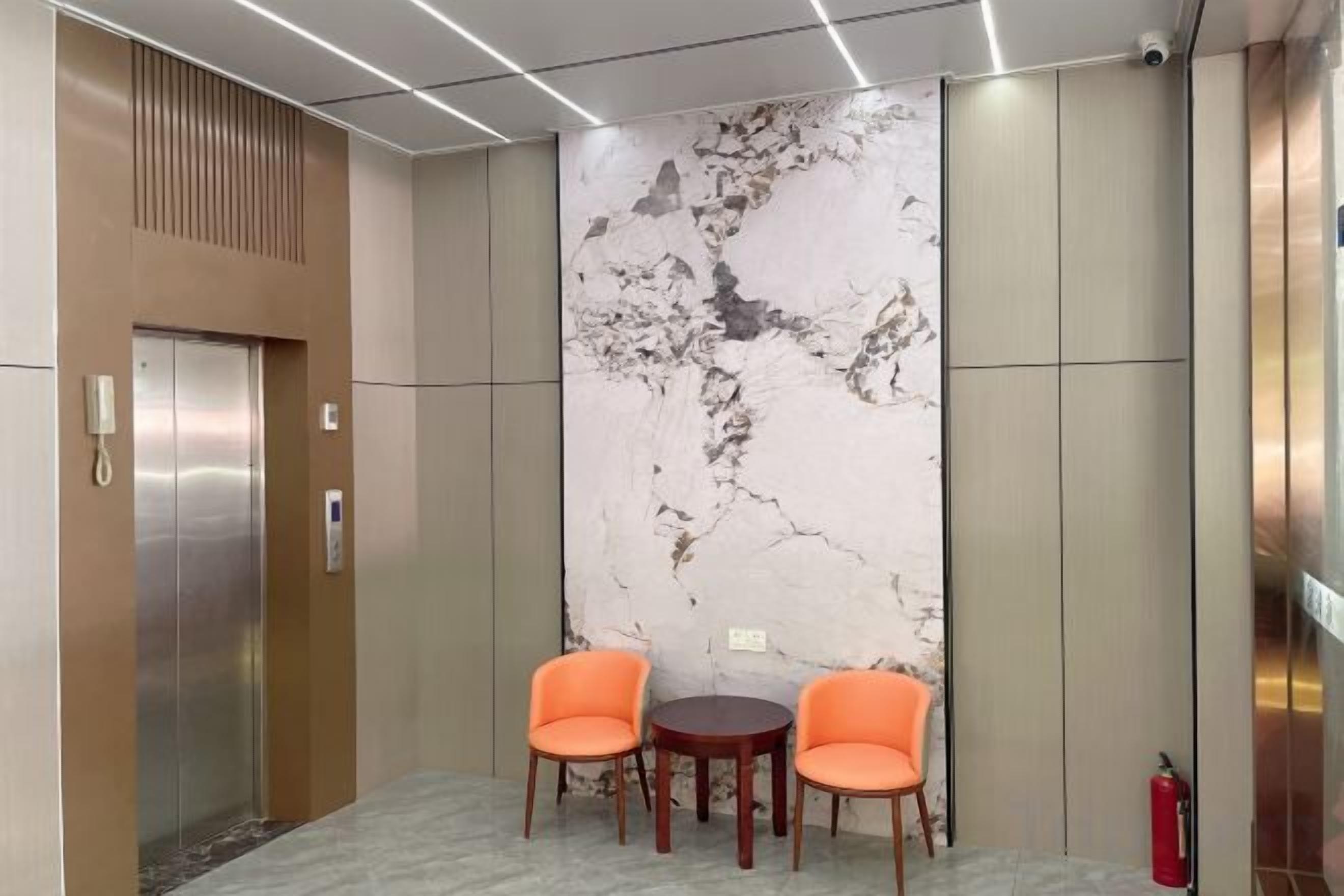 An elevator with a modern design, a marble wall, and two orange chairs.