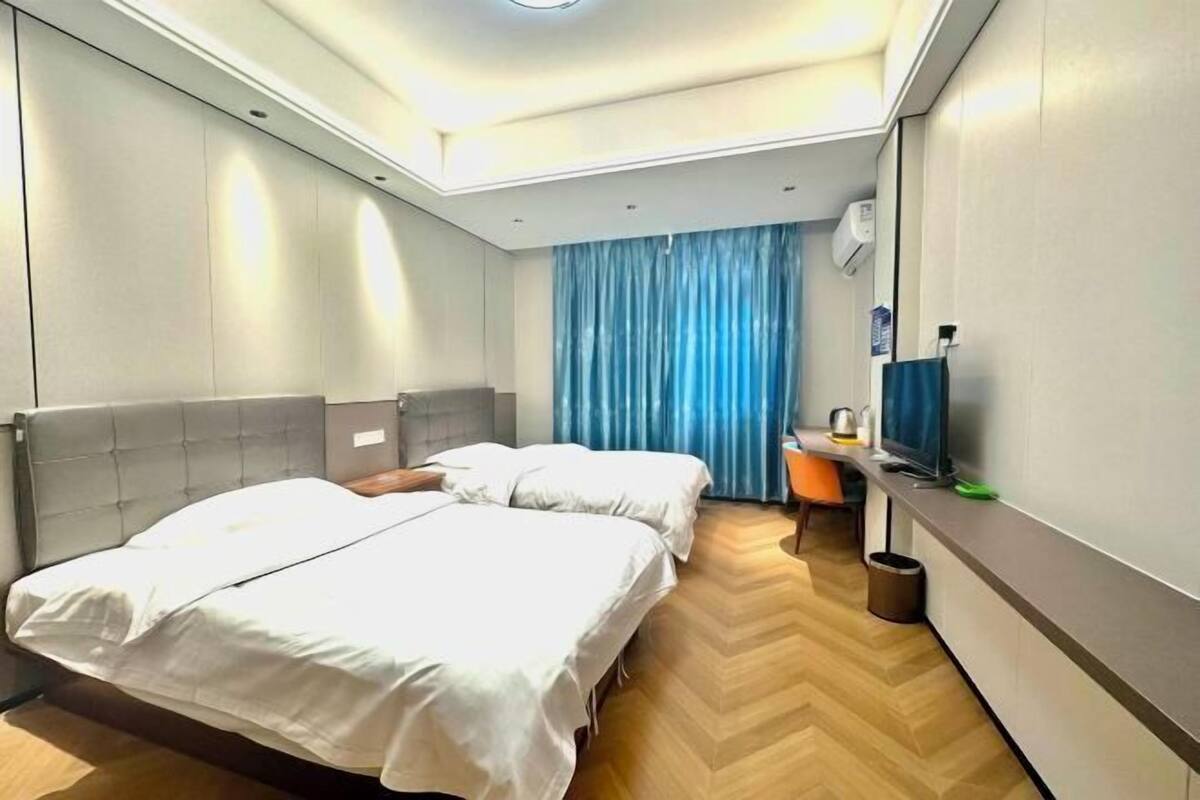 Habitación de hotel con dos camas, un escritorio con silla, televisor y ventana con cortinas azules.