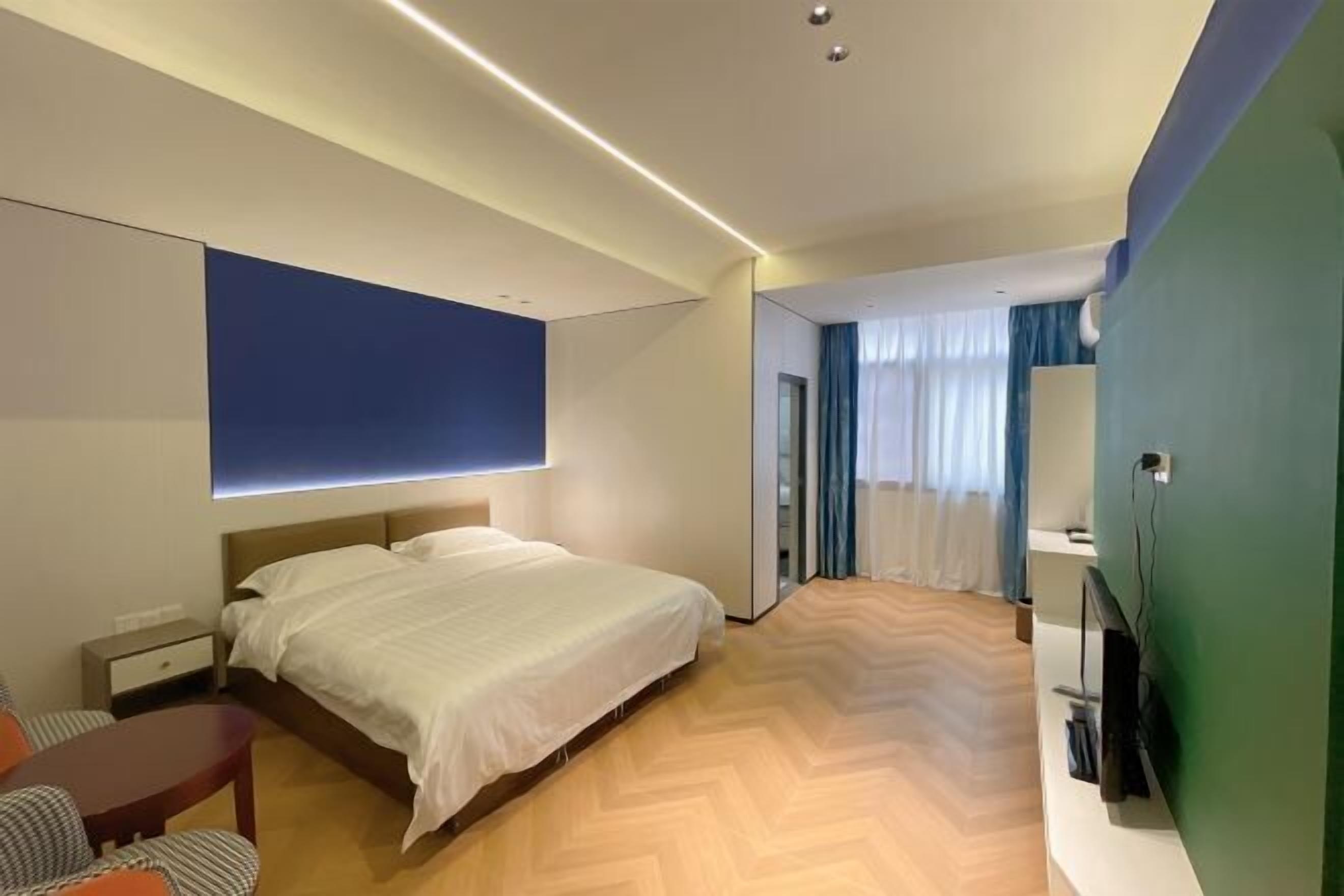 A modern hotel room with a large bed, a desk, a chair, and a TV.