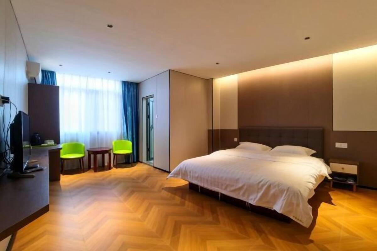 Habitación de hotel con una cama grande, un escritorio con computadora, dos sillas y un ventanal con cortinas.