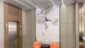 An elevator with a marble wall, two orange chairs, and a small table. - Nanning Donglian Hotel (Guangxi Police School Xianhe Campus Shop) (Nanning)