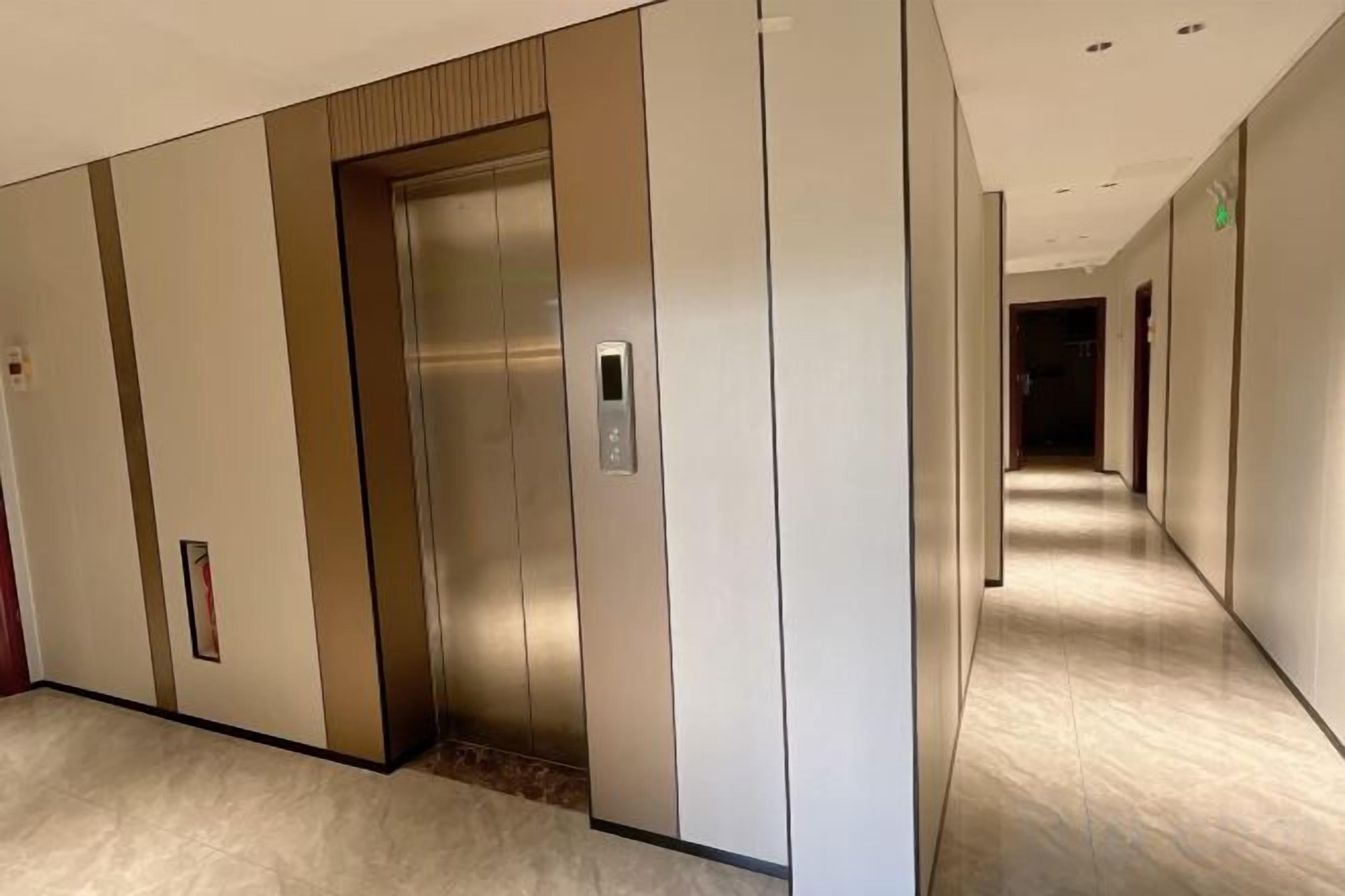 A hallway with an elevator, a door, and a corridor leading to another room.