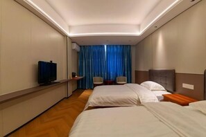 Habitación de hotel con dos camas, televisión, escritorio y ventana con cortinas azules.