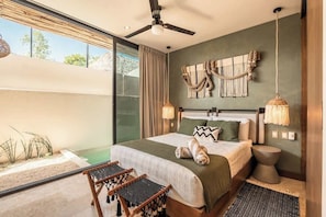 A bedroom with a bed, a ceiling fan, a large window, and a view of the outdoors.